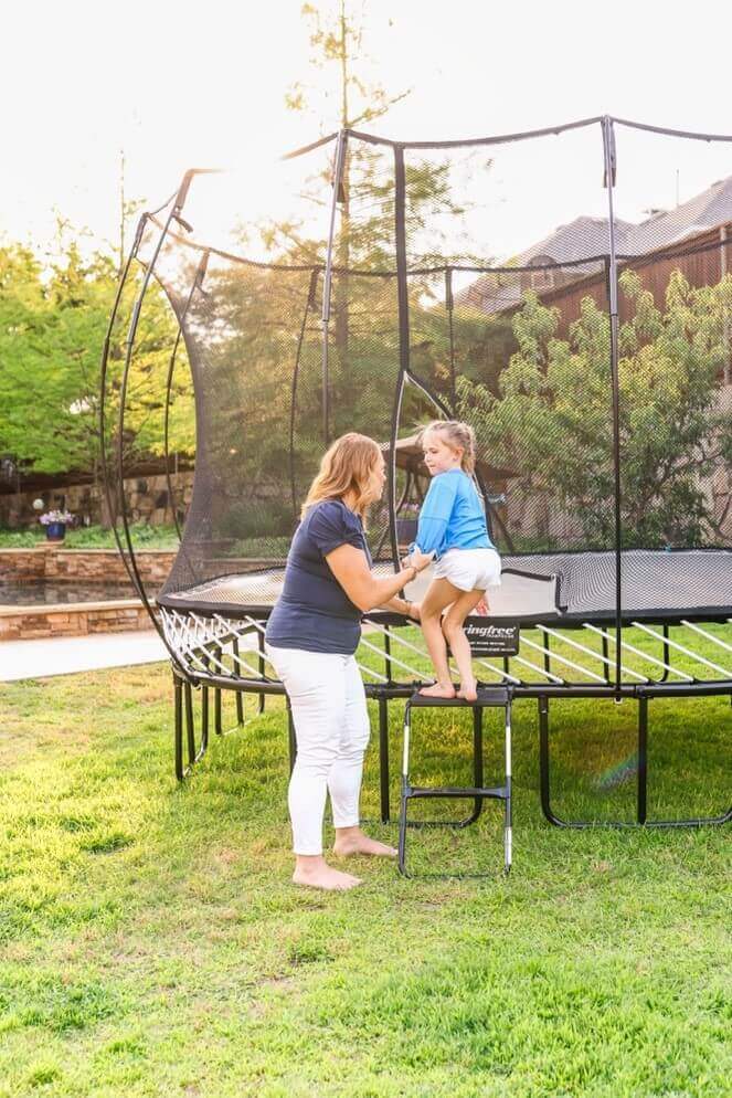 A mom helping her daughter onto a Springfree Trampoline using a ladder