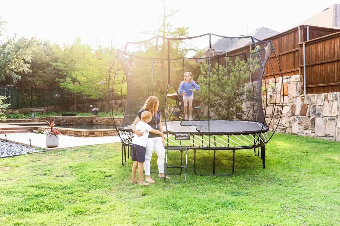 A girl jumping on a Springfree Trampoline while her mom and brother watch.