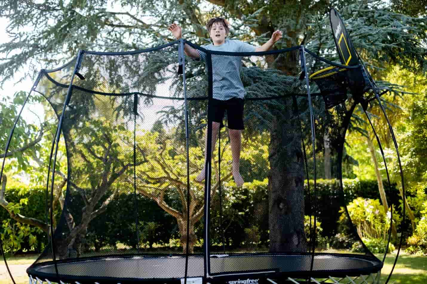 A boy jumping in mid-air on a Springfree Medium Round Trampoline with a FlexrHoop.