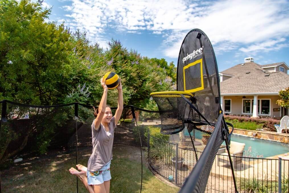 A smiling girl about to dunk on the Springfree Trampoline Basketball Hoop.
