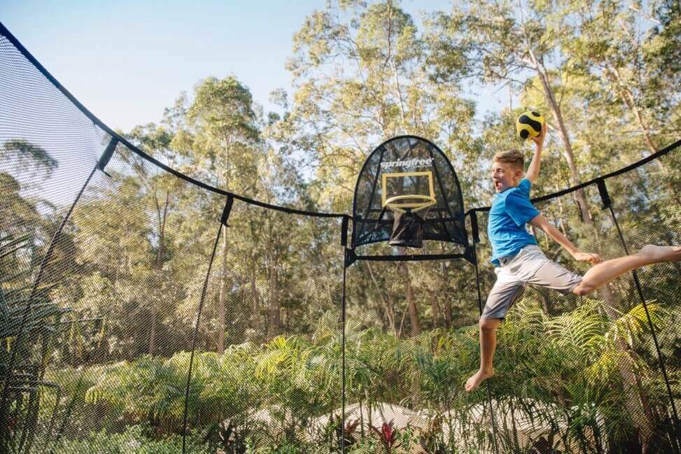 A kid dunking on a Springfree Trampoline Basketball Hoop.