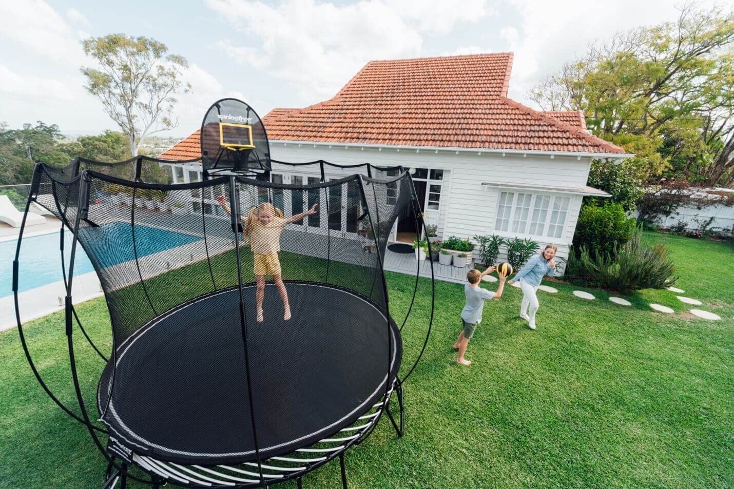 Little girl jumping on a Springfree Trampoline while her brother and mom throw a ball on the outside.