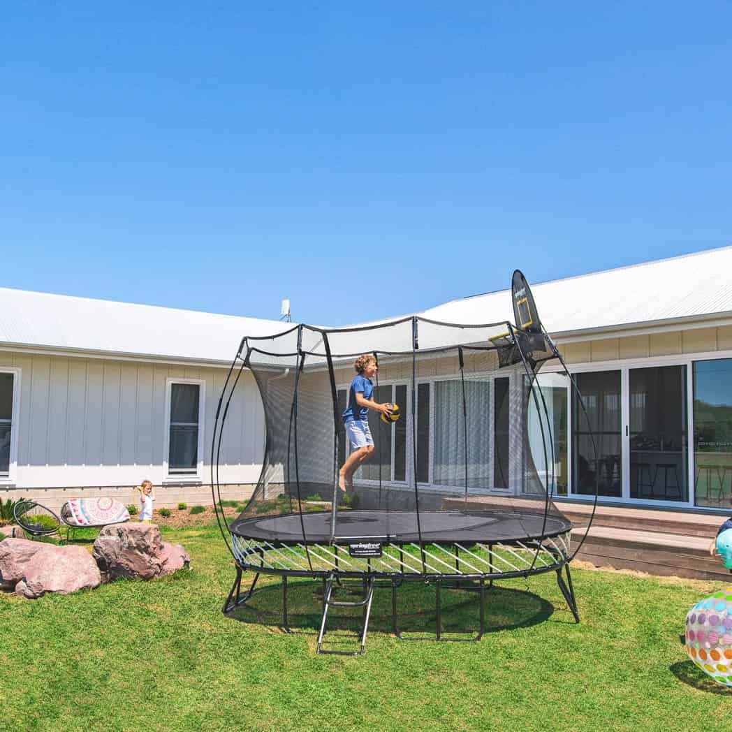 A boy dunking a ball on a Springfree Oval Trampoline.