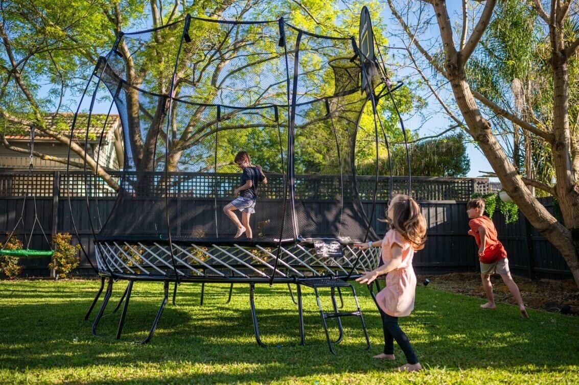 Kids playing on and around the Springfree Medium Round Trampoline.
