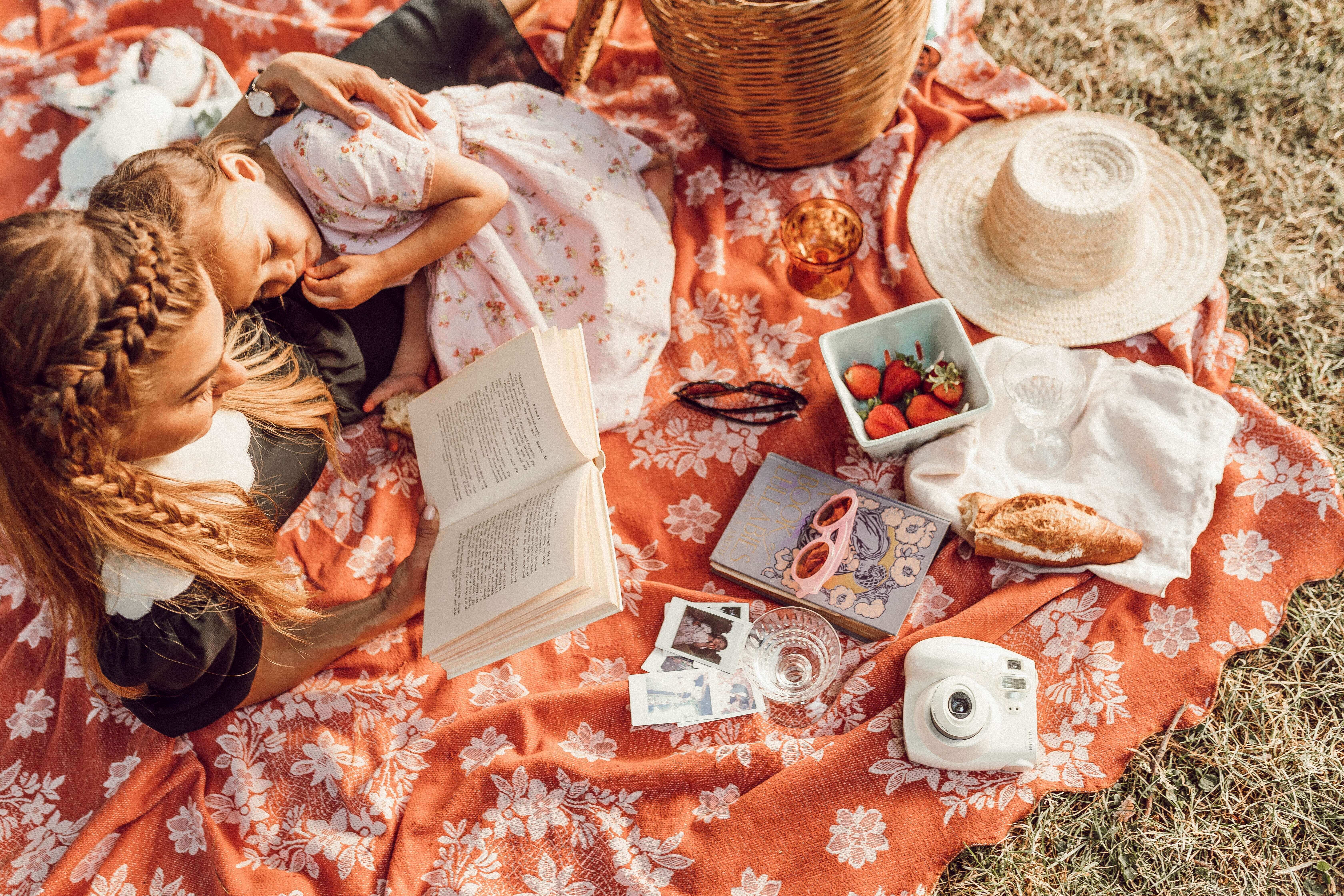 a woman and a kid reading book on a picnic