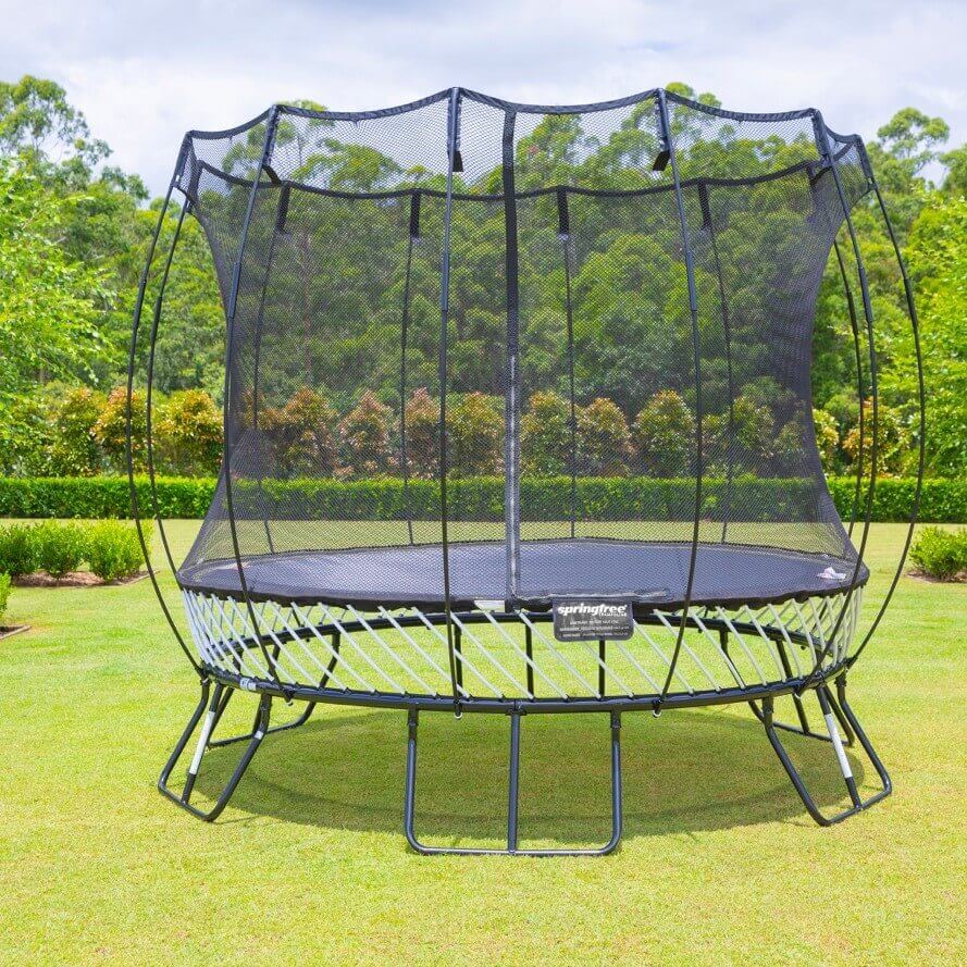 A Springfree Trampoline in a yard with bushes and trees in the background.