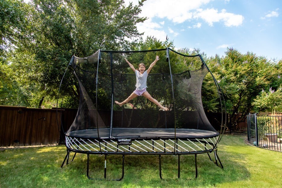 A smiling girl jumping with her limbs out on a Springfree Trampoline.