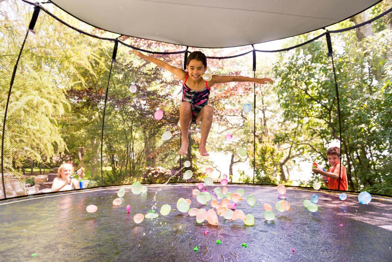 A girl jumping on a trampoline with a sunshade