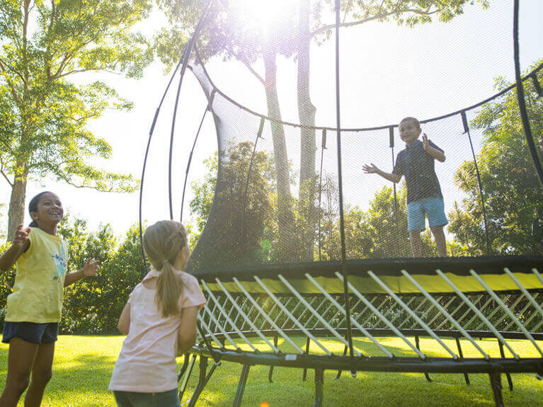 a boy inside the trampoline and two girls watching outside