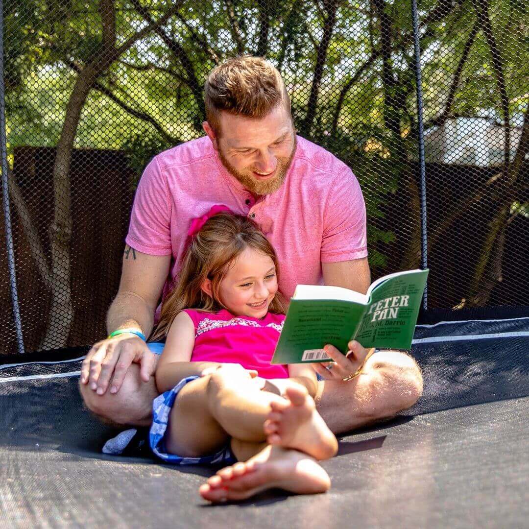 father and daughter reading book in a trampoline