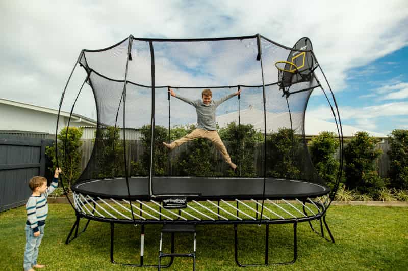 A boy jumping on a Springfree Trampoline while his brother watches from the outside.