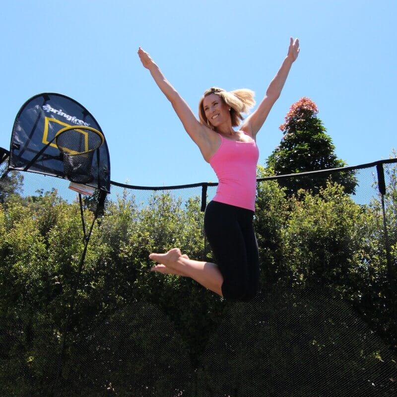 A woman in workout apparel jumping with her arms up on a Springfree Trampoline.
