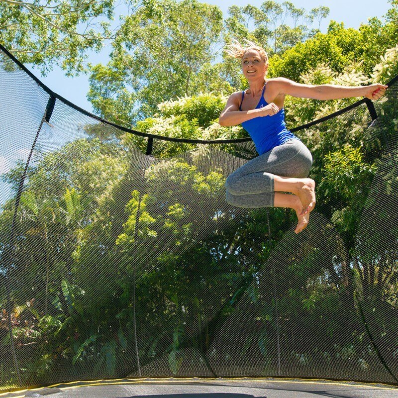 A woman in workout apparel jumping on a Springfree Trampoline with her knees to the side.