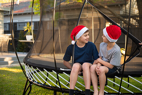 two kids wearing santa hat sitting in springfree trampoline