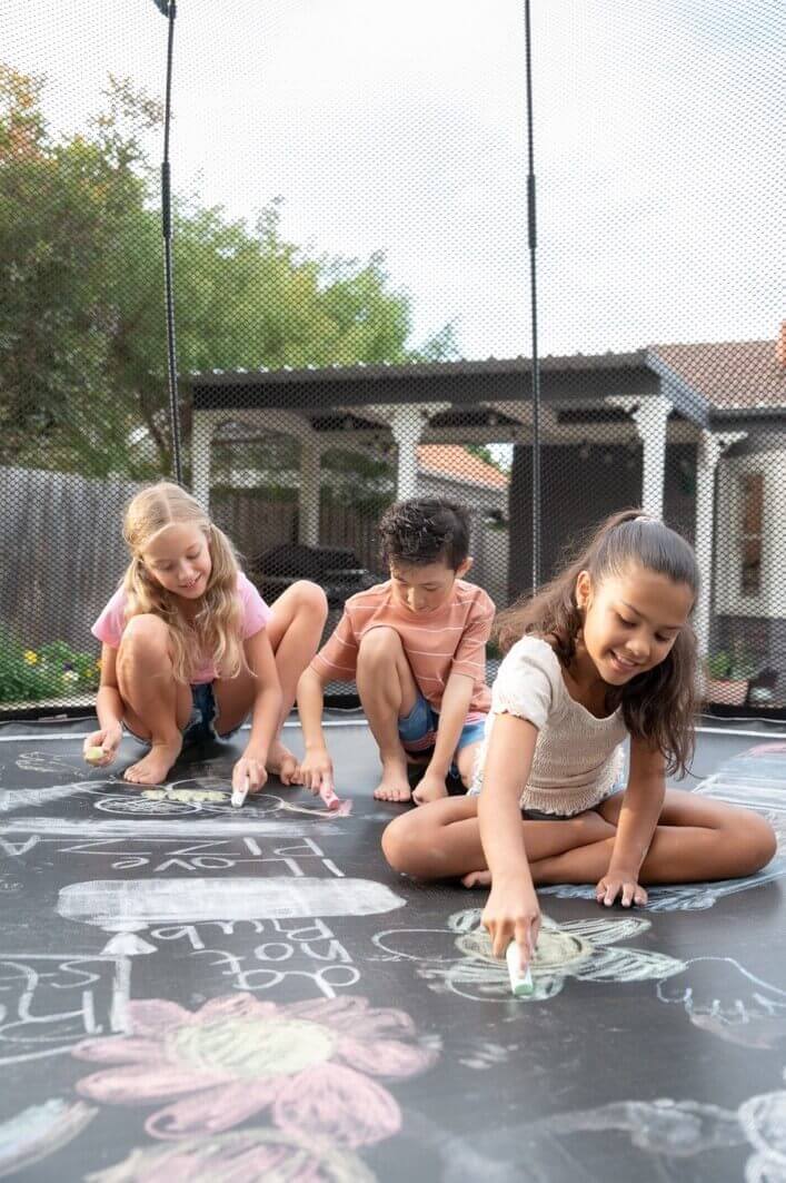 3 kids using chalk to draw on a trampoline