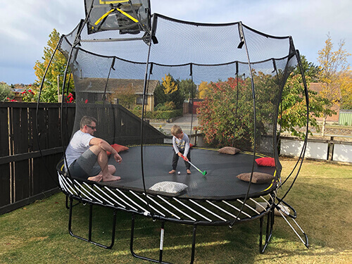a kid playing golf in a trampoline with a man watching
