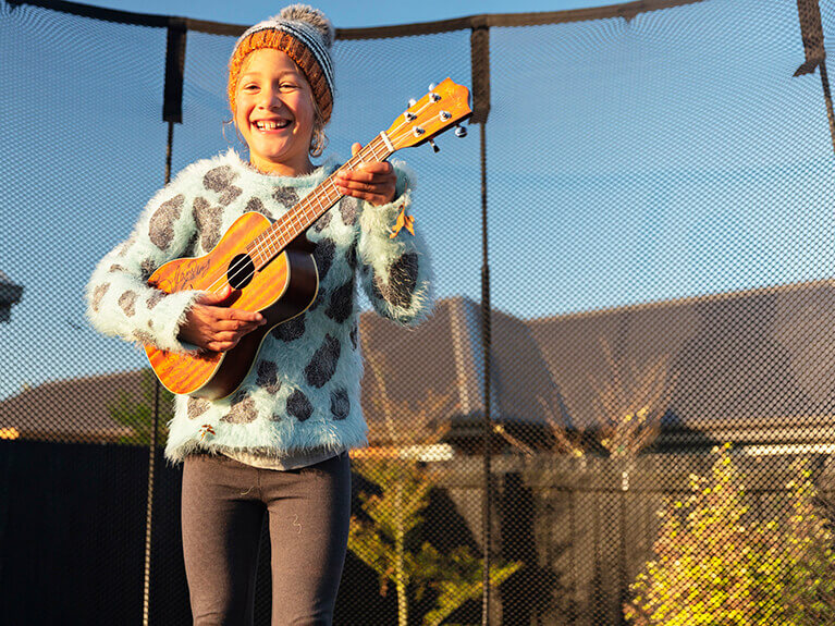 A happy girl playing a child's guitar on a trampoline.