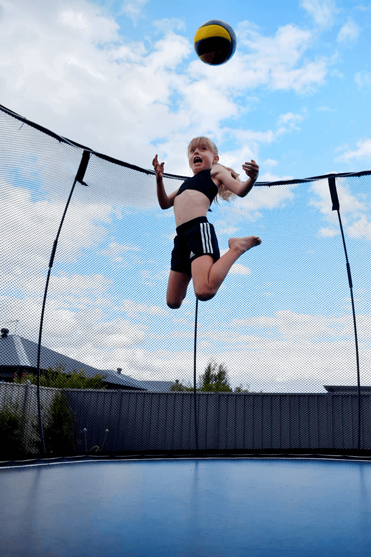 Girl in mid-air jumping on a trampoline with a ball coming at her